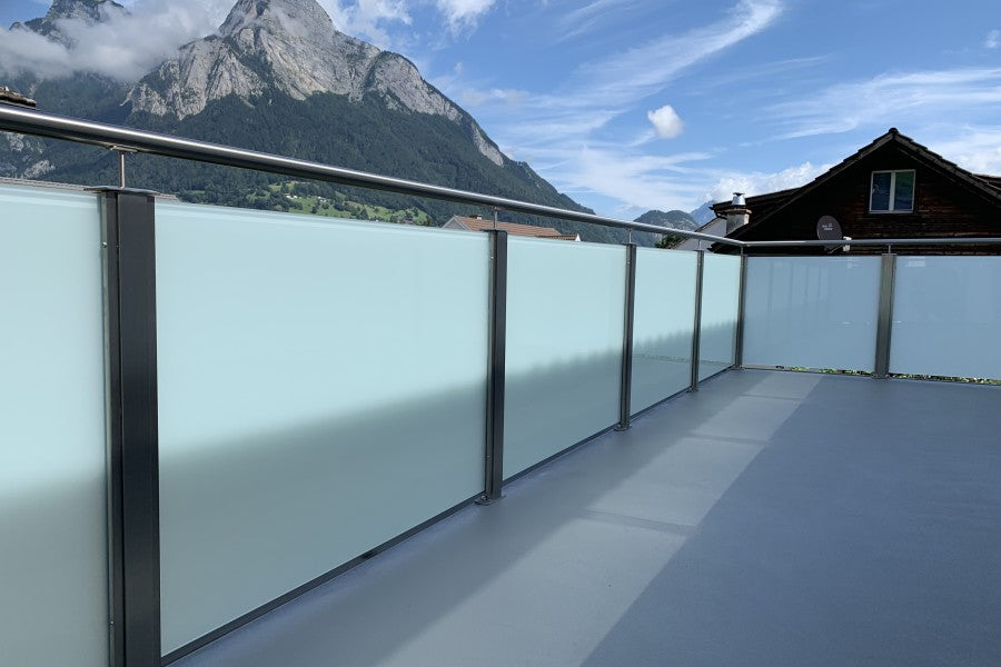 Balkongeländer aus Edelstahl mit Milchglas-Füllung vor Bergkulisse