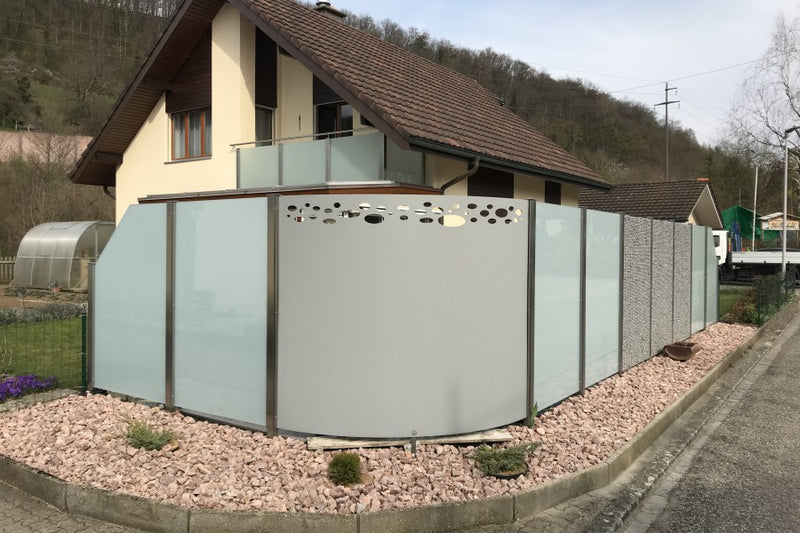 Sicht- und Windschutz aus Steinkorb, VSG-Milchglas und gerundetem Aluminiumblech mit gelasertem Sujet – Hornussen AG