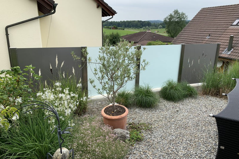Sicht- und Windschutz aus VSG-Milchglas und Aluminiumblech mit gelasertem Sujet – Fislisbach AG