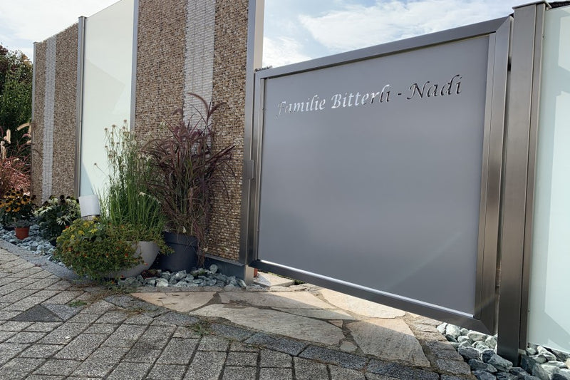 Sicht- und Windschutz mit Gartentüre aus pulverbeschichtetem Aluminiumblech, Familienname gelasert – Sisseln AG