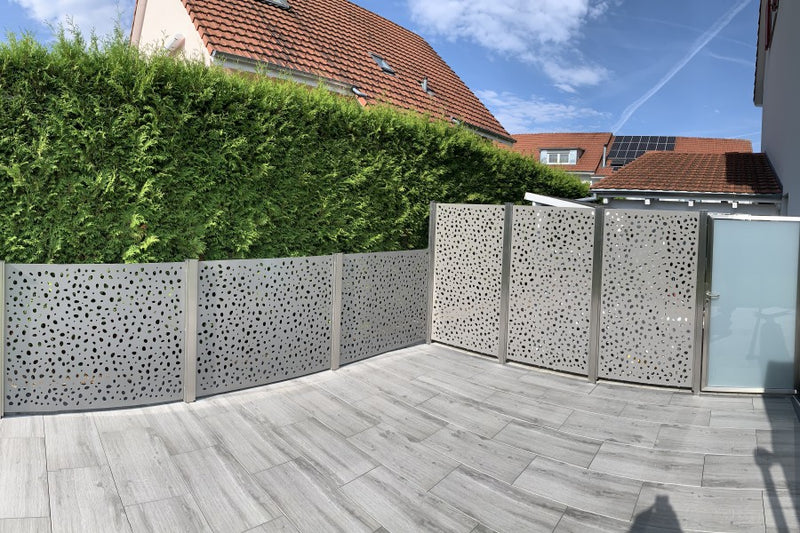 Sicht- und Windschutz aus gelasertem Aluminiumblech mit Gartentüre aus VSG-Milchglas – Herznach AG