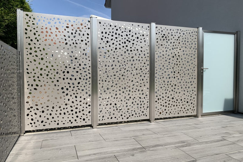 Sicht- und Windschutz aus gelasertem Aluminiumblech mit Gartentüre aus VSG-Milchglas – Herznach AG