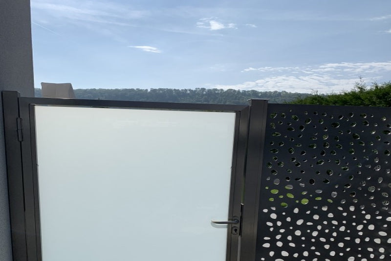 Sicht- und Windschutz aus gelasertem Aluminiumblech mit Gartentüre aus VSG-Milchglas – Herznach AG
