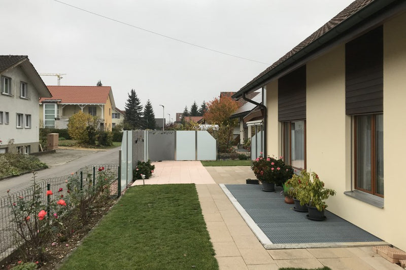 Sicht- und Windschutz aus Steinkorb, VSG-Milchglas und gerundetem Aluminiumblech mit Sujet, Lichtschacht-Abdeckung nach Mass – Hornussen AG